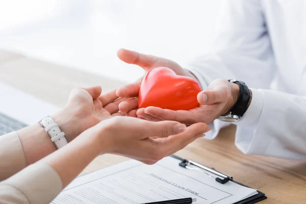 Vista recortada del médico y el paciente sosteniendo el corazón rojo en las manos, concepto de seguro médico - foto de stock