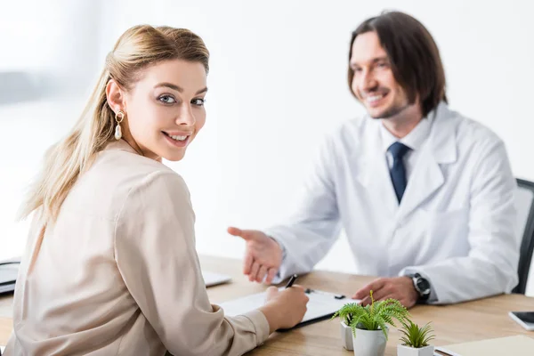 Paciente feliz médico visitante, mirando a la cámara y firmar el documento - foto de stock