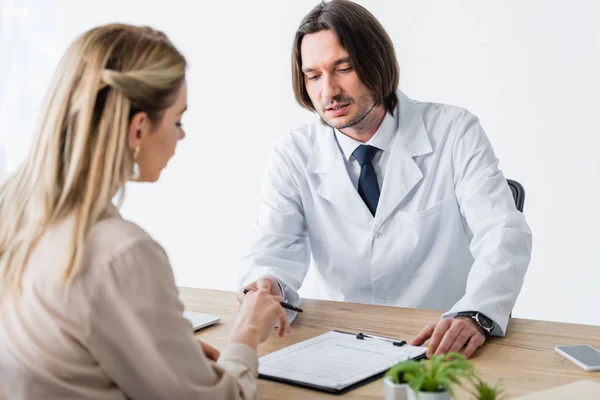 Patient sitting with doctor behind wooden table and signing document — Stock Photo