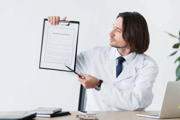 Guapo doctor en bata blanca apuntando con pluma al documento médico - foto de stock