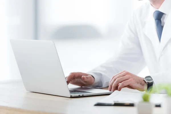 Cropped view of doctor in white coat working with laptop — Stock Photo