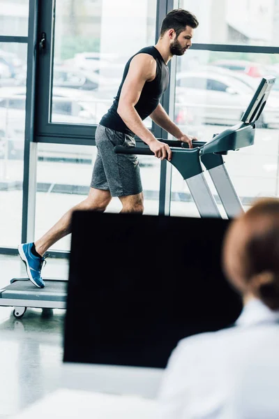 Messa a fuoco selettiva dello sportivo che corre sul tapis roulant vicino al medico durante il test di resistenza in palestra — Foto stock