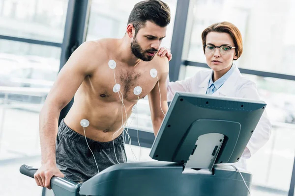Doctor conducting endurance test with sportsman in gym — Stock Photo