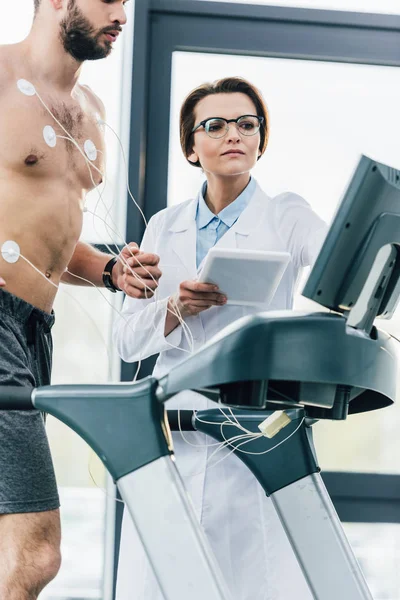 Arzt mit digitalem Tablet nahe hemdslosem Sportler beim Härtetest — Stockfoto