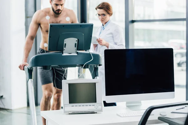 Ordenador con pantalla en blanco y médico realizando prueba de resistencia con deportista en gimnasio - foto de stock