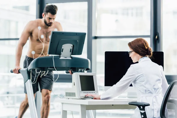 Doctor at desk conducting endurance test with sportsman in gym — Stock Photo