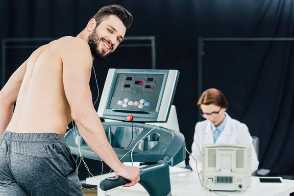 Doctor realizando prueba de resistencia con deportista sonriente en gimnasio - foto de stock