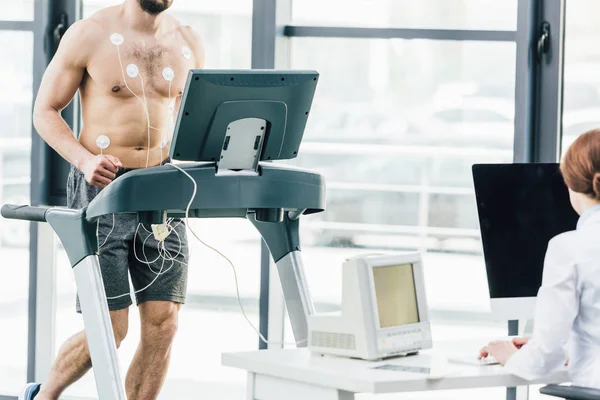 Vue partielle du médecin effectuant un test d'endurance avec un sportif au gymnase — Photo de stock