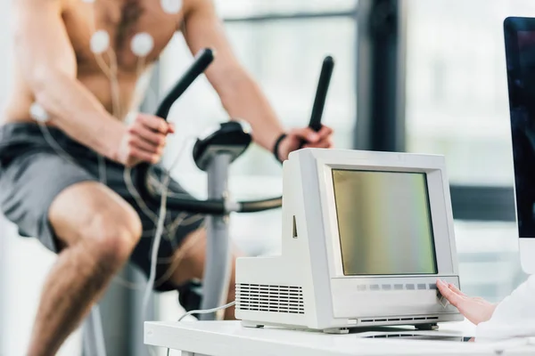 Cropped view of sportsman with electrodes training on elliptical during endurance test in gym — Stock Photo