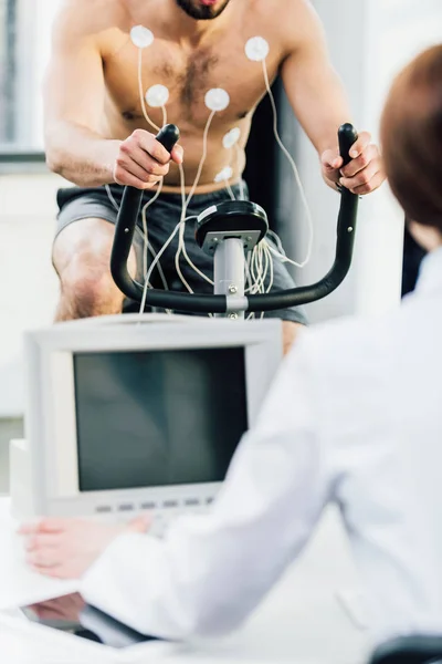 Vista recortada del médico realizando prueba de resistencia con deportista con electrodos en el gimnasio - foto de stock