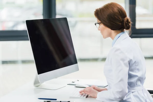 Doctor in white coat using computer with blank screen — Stock Photo