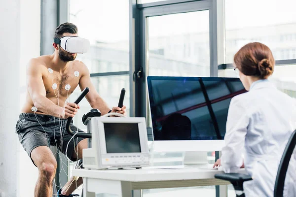 Desportista em vr fone de ouvido e médico sentado na mesa de computador durante o teste de resistência — Fotografia de Stock