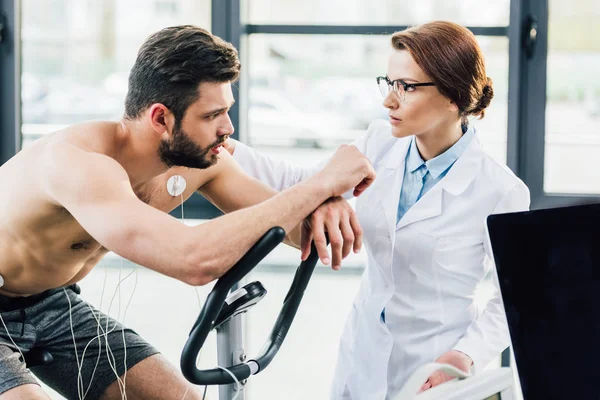 Médico cerca de deportista con electrodos en el gimnasio durante la prueba de resistencia - foto de stock