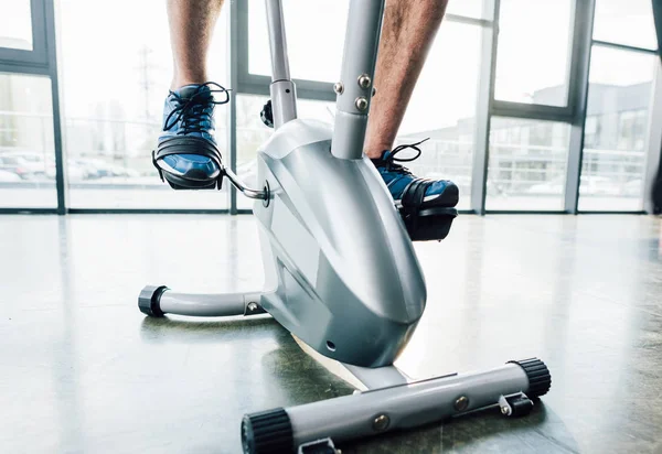 Vista recortada del entrenamiento de deportista en la máquina elíptica en el gimnasio - foto de stock