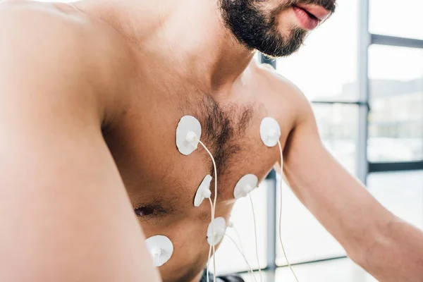 Vue recadrée du sportif avec des électrodes fonctionnant pendant l'essai d'endurance dans la salle de gym — Photo de stock