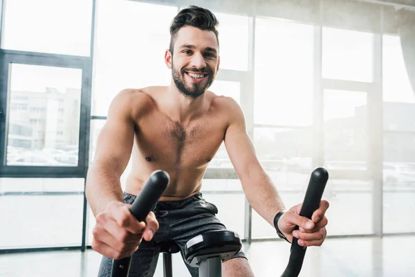 Lächelnder gutaussehender Sportler, der im Fitnessstudio auf einem Crossgerät trainiert — Stockfoto