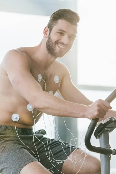 Happy handsome sportsman with electrodes on elliptical during endurance test in gym — Stock Photo