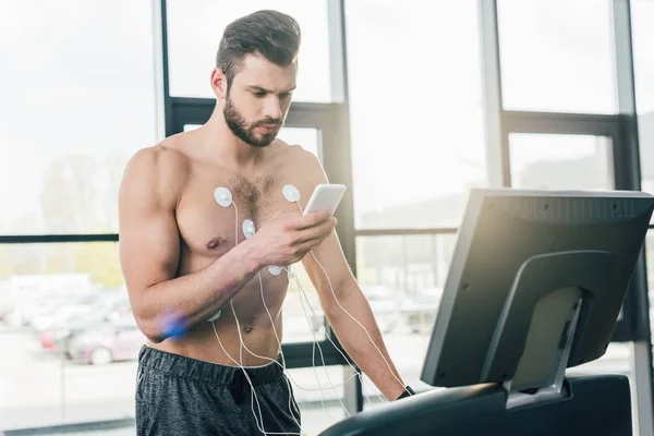 Спортсмен зі смартфоном, що працює на біговій доріжці під час тесту на витривалість у спортзалі — стокове фото