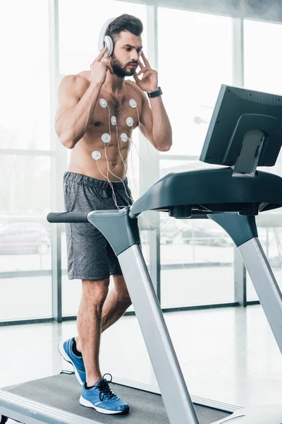 Мускулистый спортсмен в наушниках, работающий на беговой дорожке во время испытаний на выносливость в спорткомплексе — стоковое фото