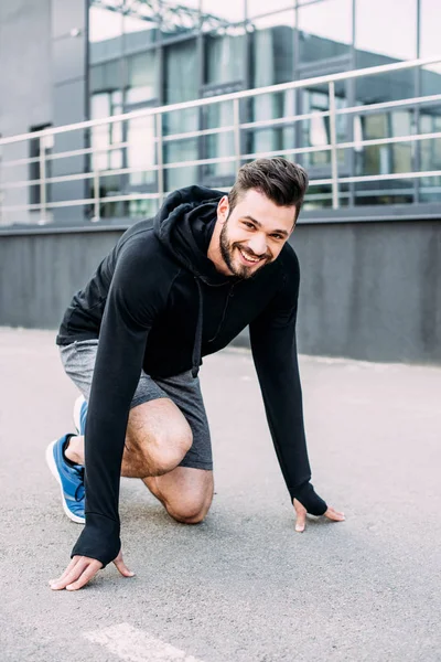 Lächelnder gutaussehender Sportler in Startposition bereit zum Laufen — Stockfoto