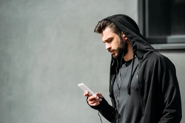 Homem com capuz e fones de ouvido usando smartphone em cinza com espaço de cópia — Fotografia de Stock