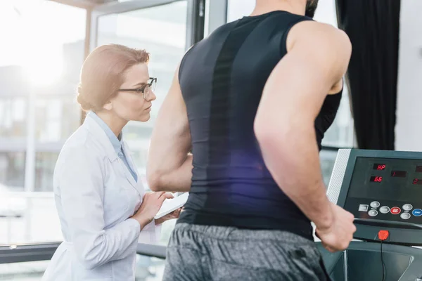 Allenamento sportivo sul tapis roulant vicino al medico durante il test di resistenza in palestra — Foto stock