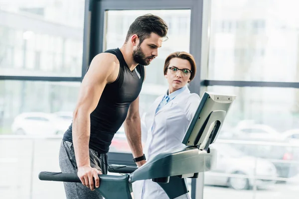 Sportsman training on treadmill near doctor during endurance test in gym — Stock Photo