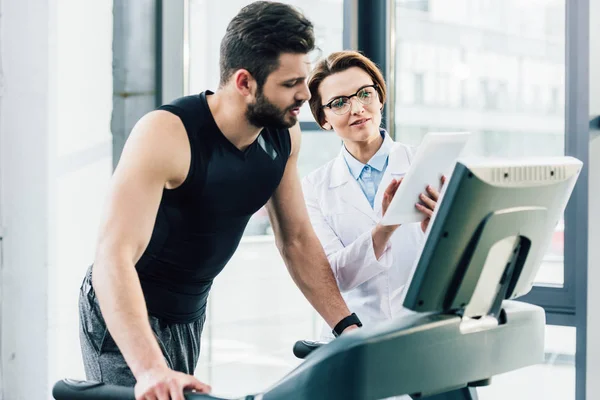 Sportivo che lavora sul tapis roulant vicino al medico durante il test di resistenza in palestra — Foto stock