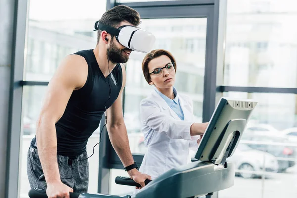 Sportsman in vr headset training on treadmill near doctor during endurance test in gym — Stock Photo