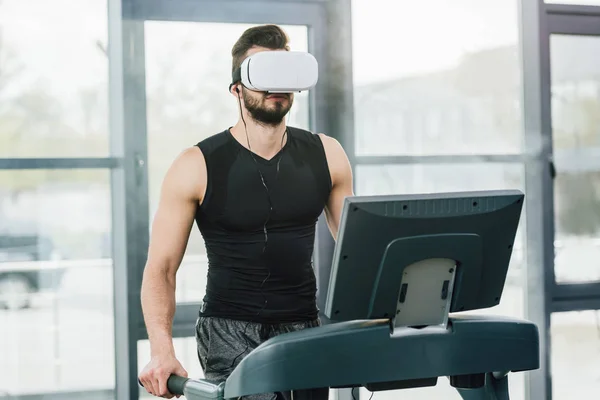 Спортсмен в наушниках виртуальной реальности работает на беговой дорожке в тренажерном зале — стоковое фото