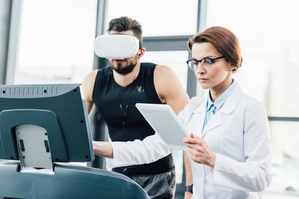 Desportista em realidade virtual fone de ouvido correndo em esteira perto médico durante teste de resistência — Fotografia de Stock