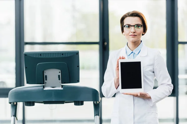 Doctor in white coat presenting Digital Tablet with blank screen at gym — Stock Photo