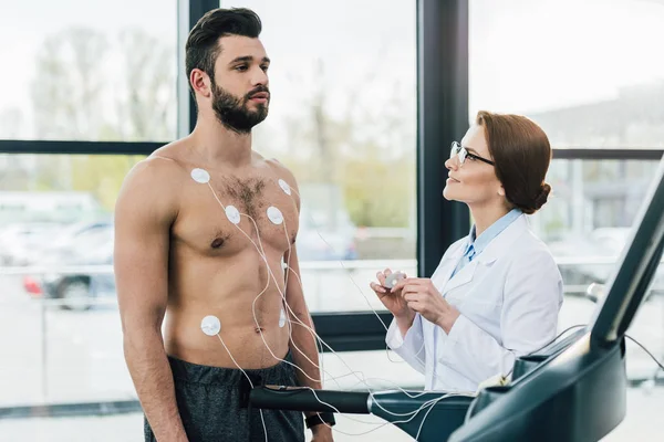 Doctor realizando prueba de resistencia cerca de deportista con electrodos en centro deportivo - foto de stock