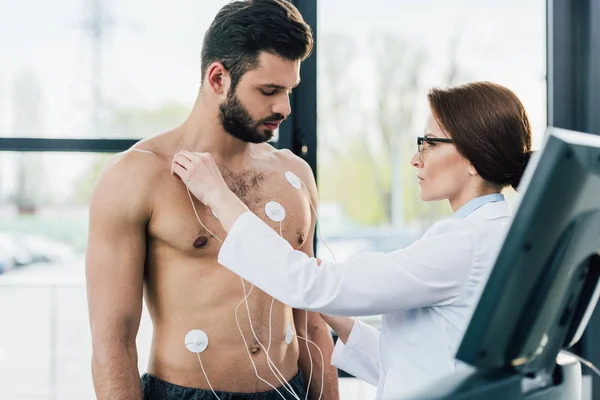 Доктор надевает электроды на человека без рубашки во время теста на выносливость — стоковое фото