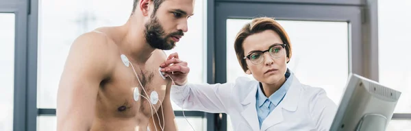 Panoramaaufnahme eines Arztes, der bei einem Härtetest Elektroden auf einen hemdlosen Mann legt — Stockfoto
