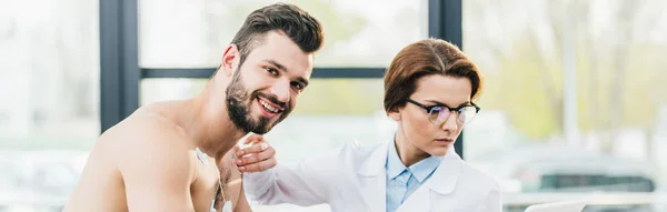 Panoramaaufnahme eines Arztes, der während eines Härtetests Elektroden auf lächelnden, hemdslosen Mann legt — Stockfoto