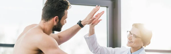 Tiro panorámico de médico dando cinco a un hombre sin camisa - foto de stock