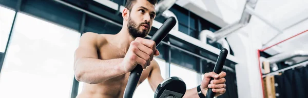 Plano panorámico del entrenamiento de deportista guapo en máquina elíptica en el gimnasio - foto de stock