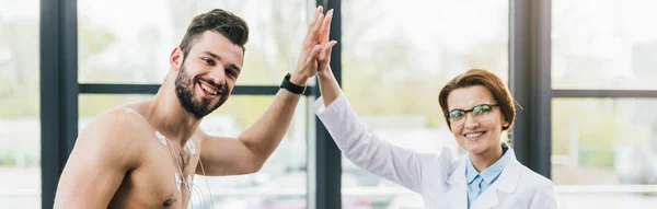 Tiro panorámico de médico dando cinco a un hombre sin camisa - foto de stock