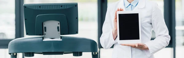 Tiro panorâmico de médico de casaco branco apresentando Digital Tablet com tela em branco no ginásio — Fotografia de Stock