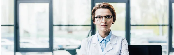 Panoramaaufnahme der schönen Ärztin im weißen Mantel, die in die Kamera blickt — Stockfoto