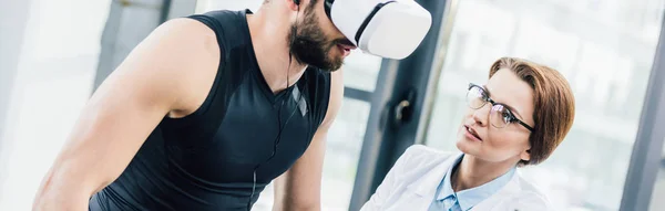 Prise de vue panoramique du médecin et sportif avec casque de réalité virtuelle dans la salle de gym — Photo de stock