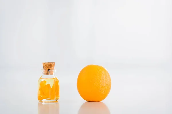 Whole orange near corked glass bottle with essential oil on white background — Stock Photo