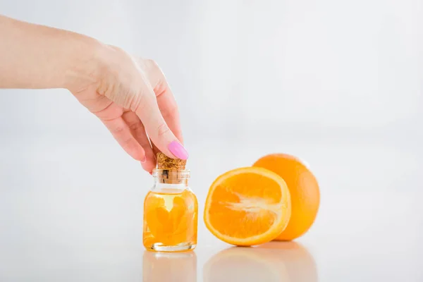 Vista parcial de la mujer botella de vidrio de corcho con aceite esencial de naranja cerca de naranjas frescas sobre fondo blanco - foto de stock