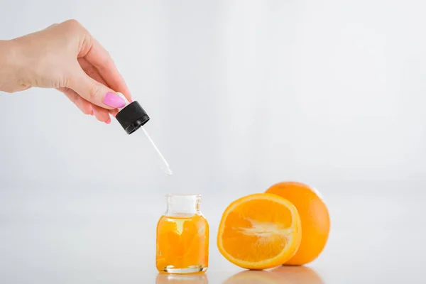 Vista recortada de la mujer sosteniendo cayó cerca de botella con aceite esencial de naranja y naranjas frescas sobre fondo blanco - foto de stock