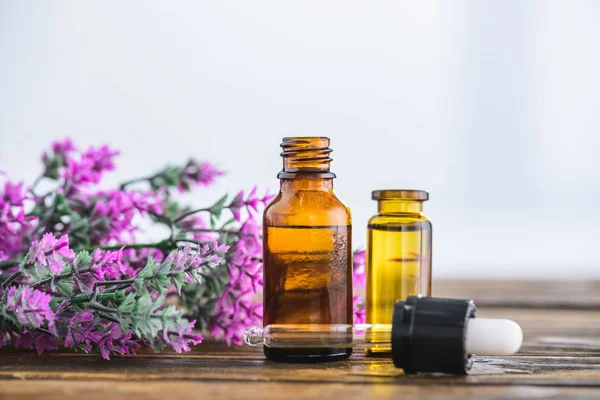 Bottles with essential oils, dropper and heather flowers on white background — Stock Photo