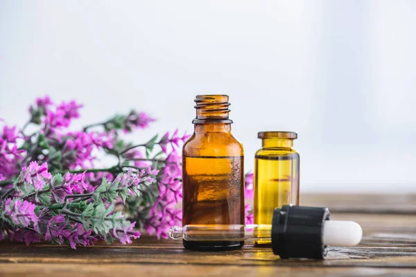 Bouteilles avec huiles essentielles, compte-gouttes et fleurs de bruyère sur fond blanc — Photo de stock