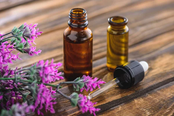 Bottles with essential oils, dropper and heather plant on wooden surface — Stock Photo