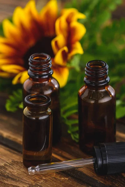 Bouteilles avec huiles essentielles, compte-gouttes et tournesol sur surface en bois — Photo de stock