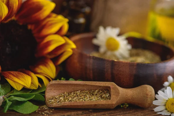 Selective focus of wooden spatula with dried herbs, sunflower and chamomile flowers on wooden surface — Stock Photo